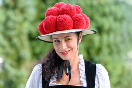 Attractive young woman wearing a traditional Black Forest Bollenhut with its 14 pompoms as she smiles at the camera outdoors against greenery