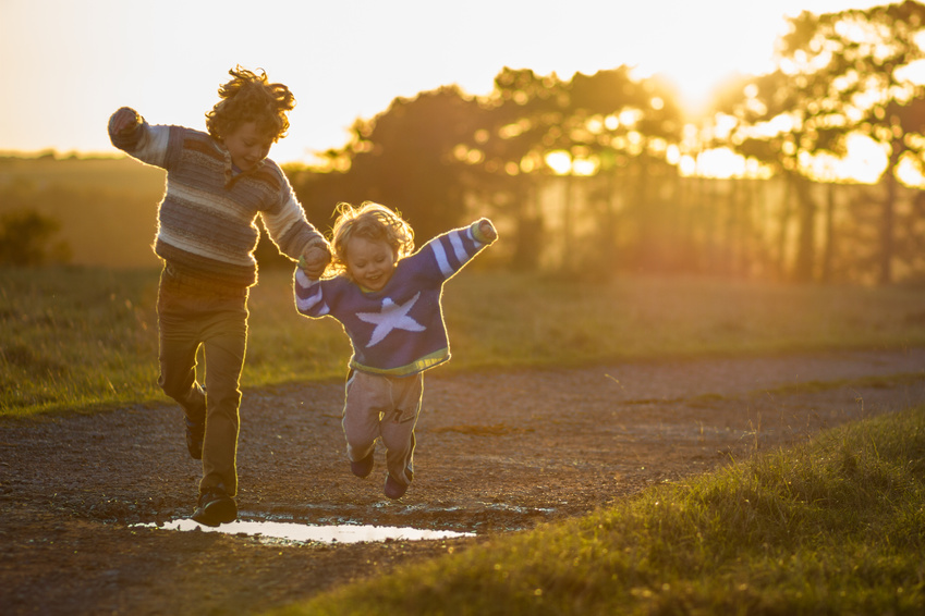 two young borthers holding hands and jumping over a puddle at sunset